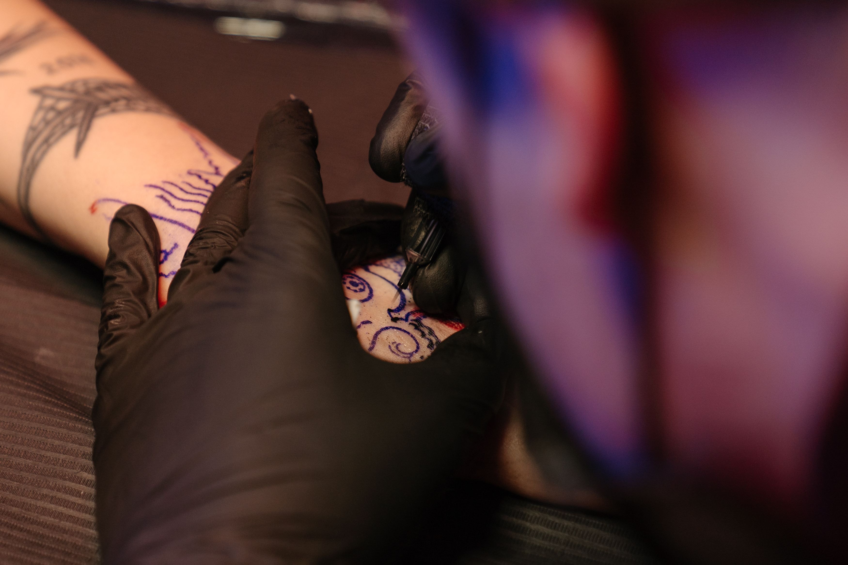 Sesión de tatuaje: manos con guantes negros delineando un diseño sobre la piel